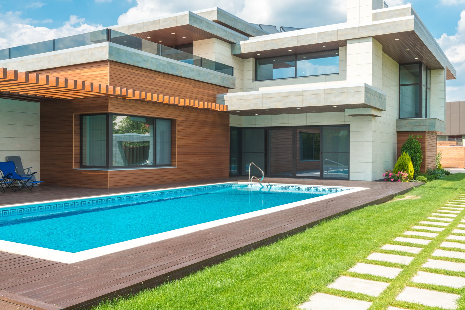 A rectangular residential pool and its deck behind a modern house, lawn beyond