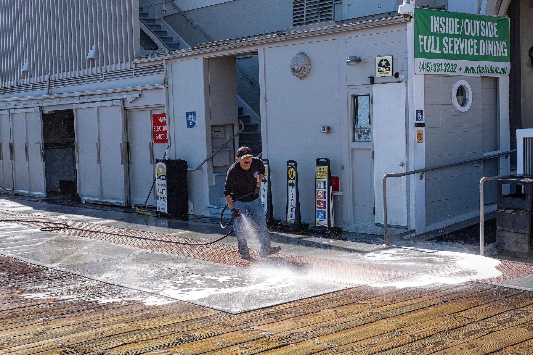 A worker washing a concrete walkway with a pressure lance, water spraying across the slab