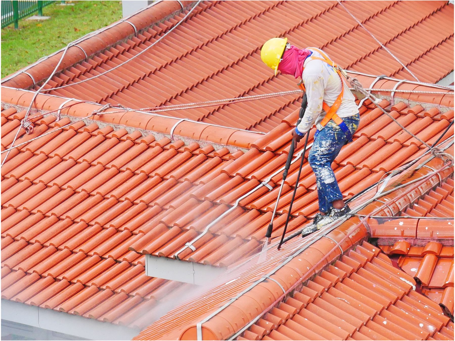 A worker pressure-cleaning a roof slope
