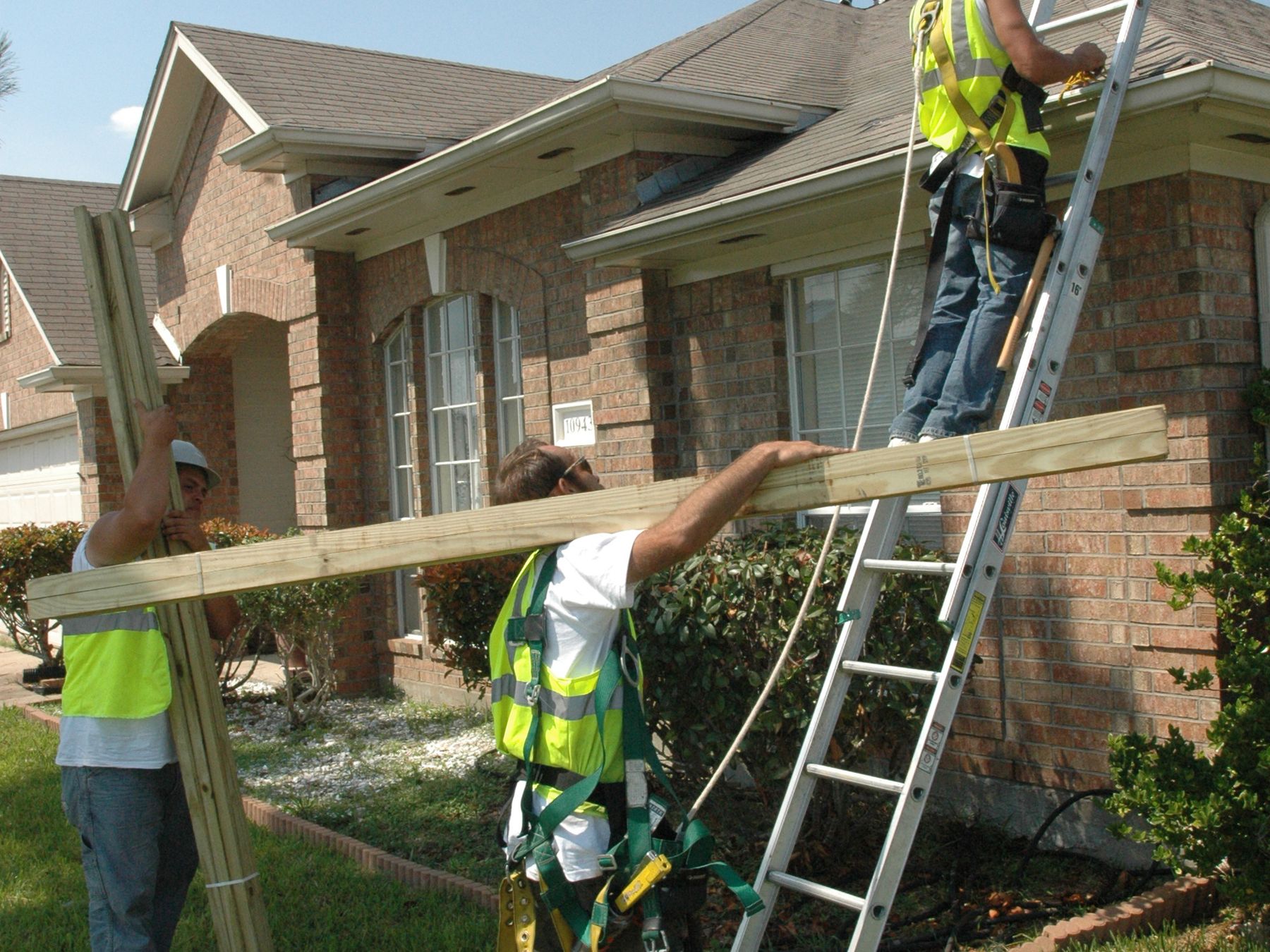 A roofing crew carrying timber up to a roof