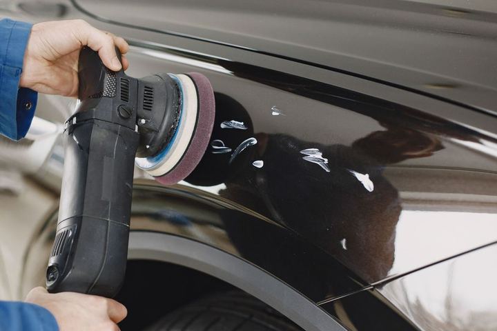 Hands polishing the fresh clear coat on a black car's front fender
